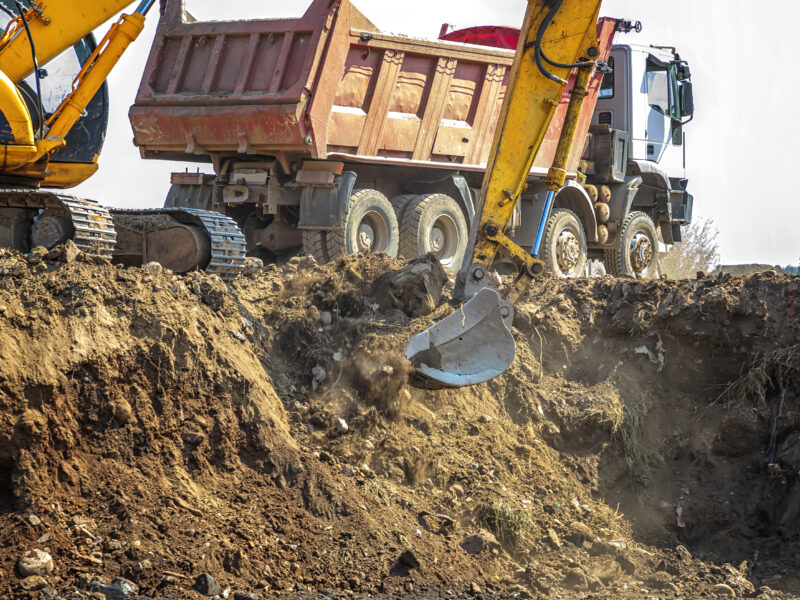 Excavator is loading excavation on the truck. Heavy construction equipment consisting of a boom, dipper or stick, bucket, and cab on a rotating platform.